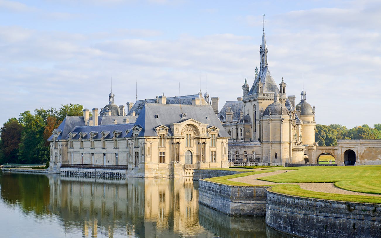 Chateau of Chantilly reflecting in water, showcasing its grand architecture.