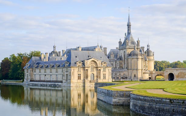 Chateau of Chantilly reflecting in water, showcasing its grand architecture.