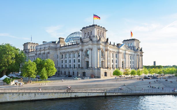 Reichstag building in Berlin with glass dome and German flags.