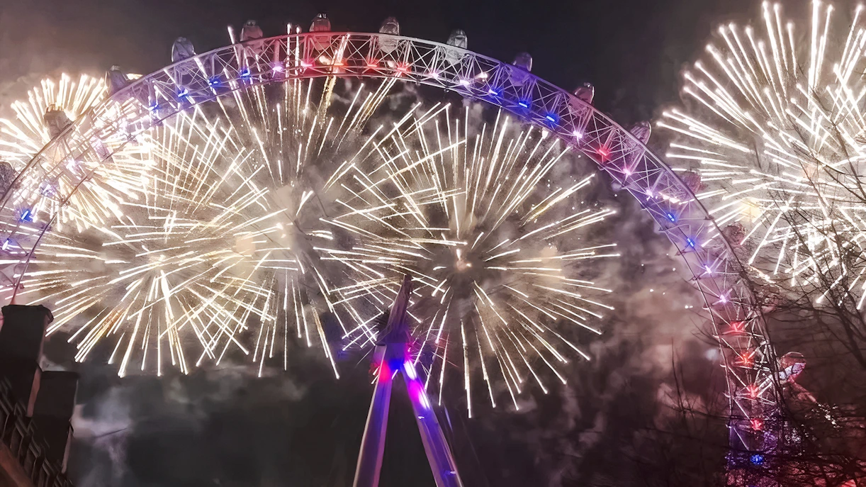 London Eye illuminated by fireworks during New Year's celebration.