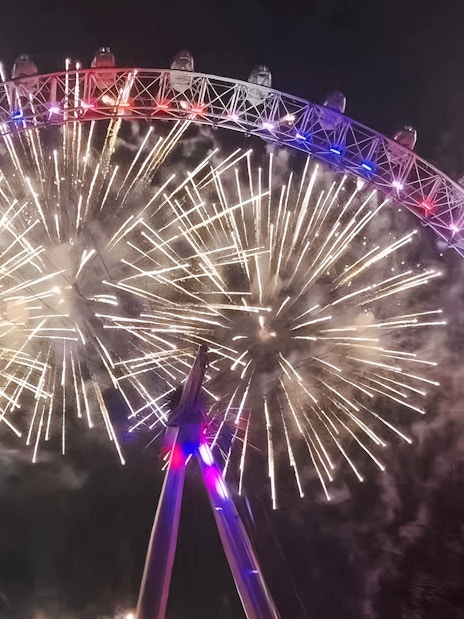 London Eye illuminated by fireworks during New Year's celebration.