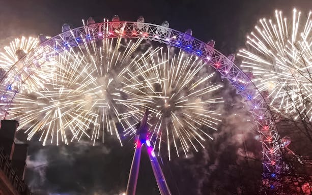 London Eye illuminated by fireworks during New Year's celebration.