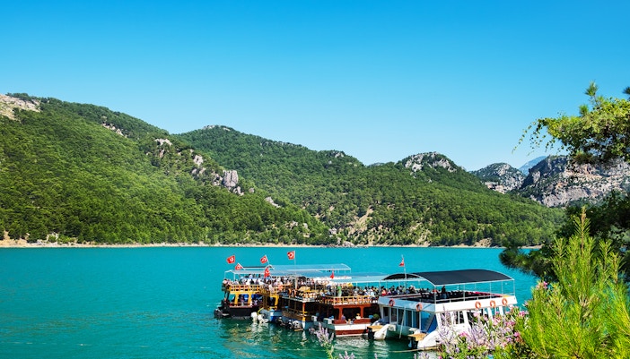 Green Canyon boat navigating turquoise waters with lush cliffs, Antalya.