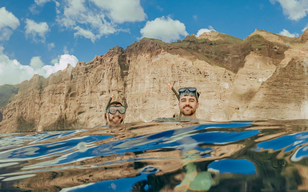 Snorkelers in clear Tenerife waters with rocky cliffs in the background.