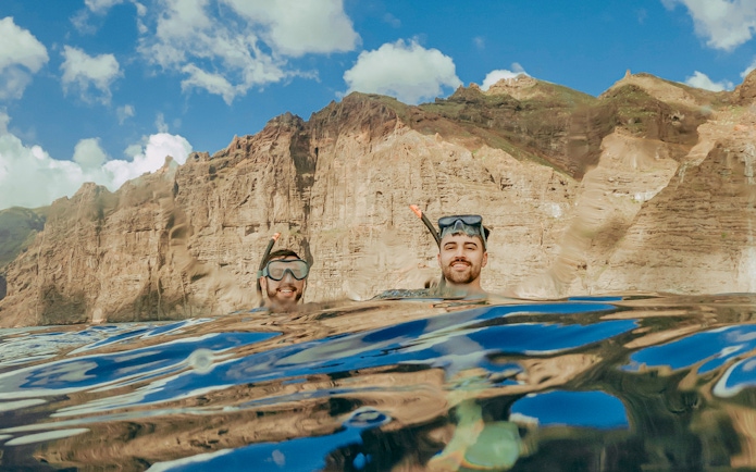 Snorkelers in clear Tenerife waters with rocky cliffs in the background.