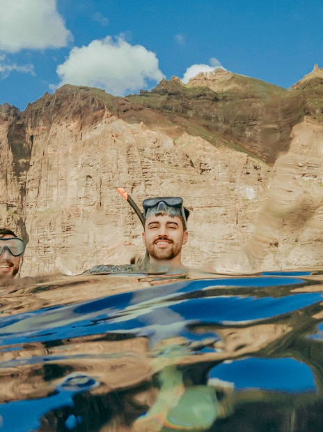 Snorkelers in clear Tenerife waters with rocky cliffs in the background.