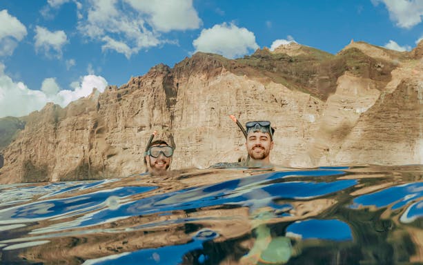 Snorkelers in clear Tenerife waters with rocky cliffs in the background.