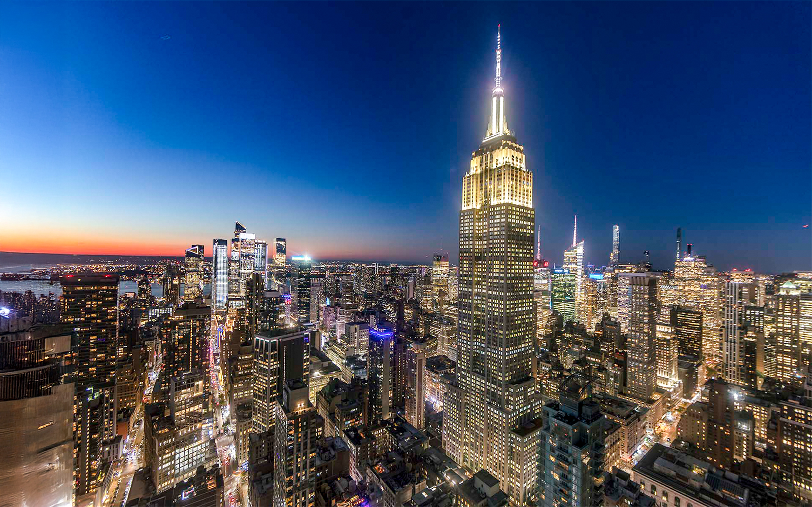 Empire State Building illuminated at night, overlooking New York City skyline.