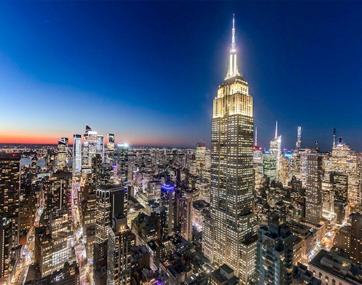 Empire State Building illuminated at night, overlooking New York City skyline.