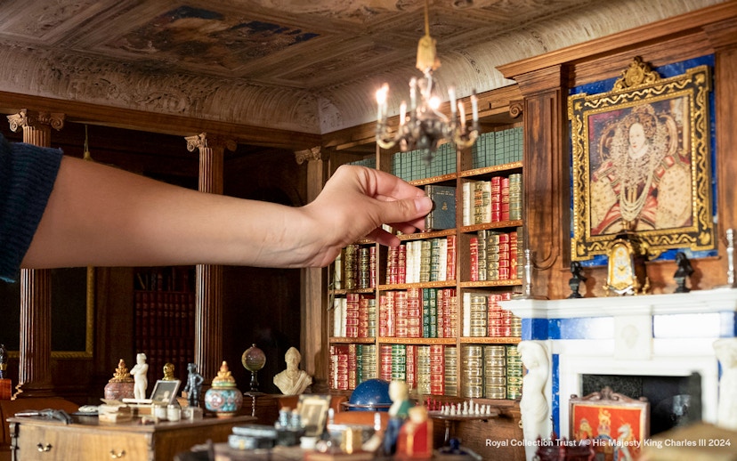 Hand arranging miniature books in Windsor Castle library model.