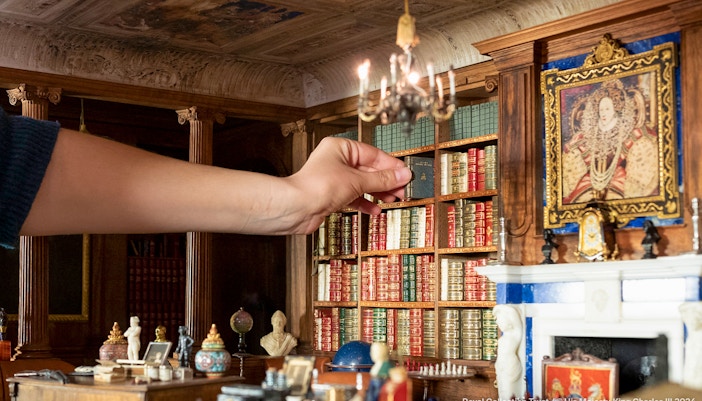 Hand arranging miniature books in Windsor Castle library model.