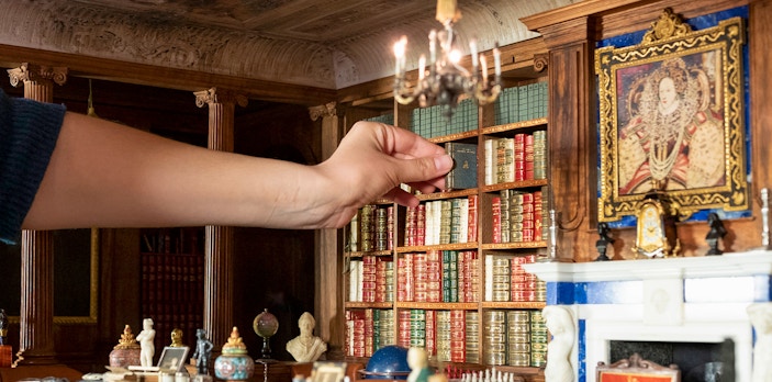 Hand arranging miniature books in Windsor Castle library model.