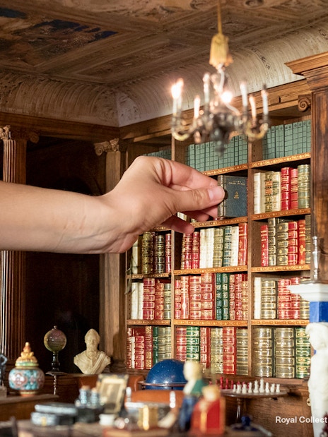 Hand arranging miniature books in Windsor Castle library model.