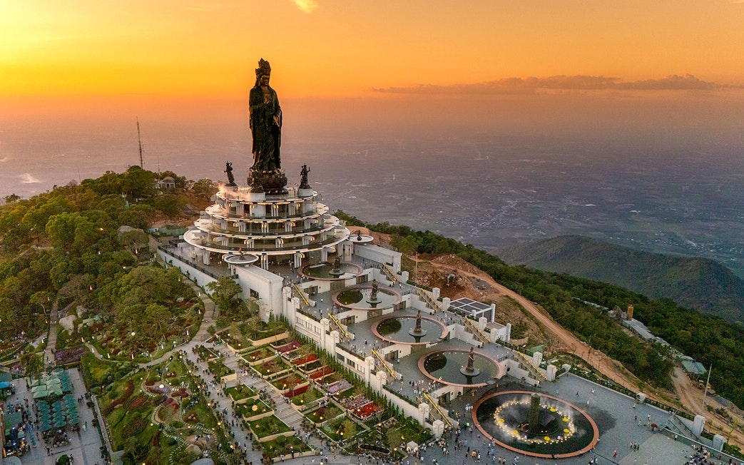 Guanyin statue in Tay Ninh province at sunset with surrounding gardens and visitors.