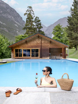 Woman relaxing in QC Terme Bagni Nuovi pool with mountains in the background.