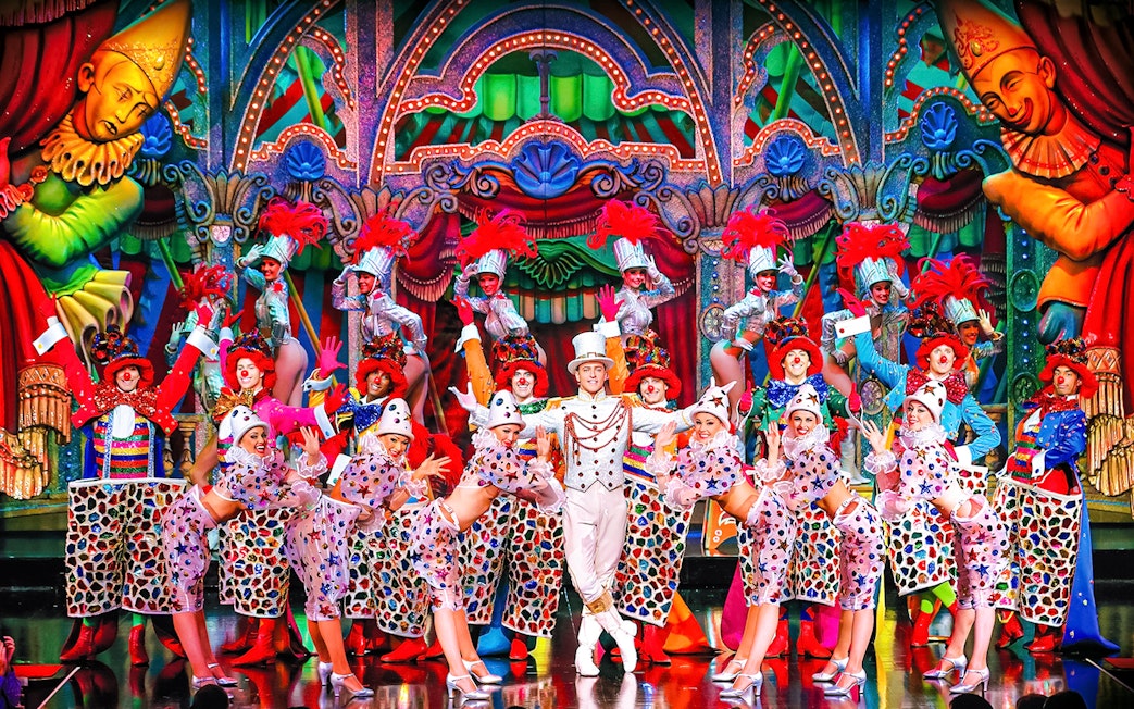 Performers in colorful costumes on stage at the Moulin Rouge show in Paris.
