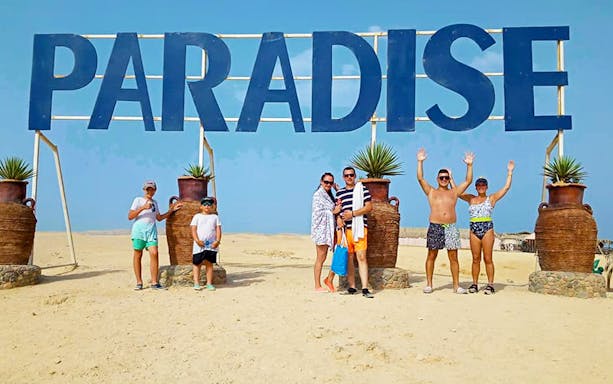Group of tourists under "Paradise" sign on Paradise Island during snorkeling sea tour from Hurghada.