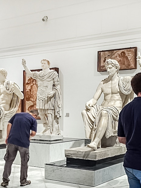 Visitors viewing classical statues at Naples National Archaeological Museum.