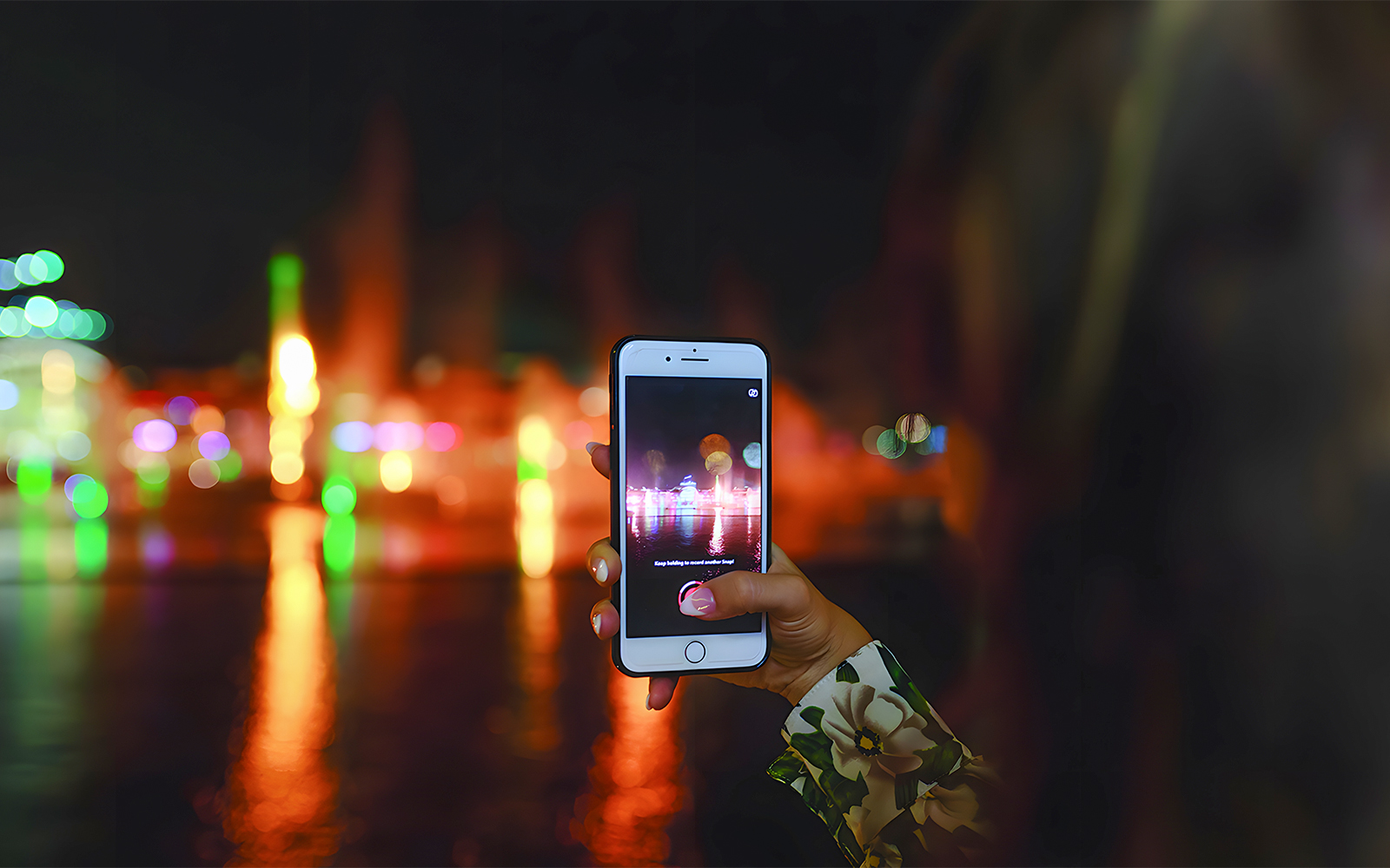 Hand holding a phone capturing Dubai Water Canal lights during dinner cruise.