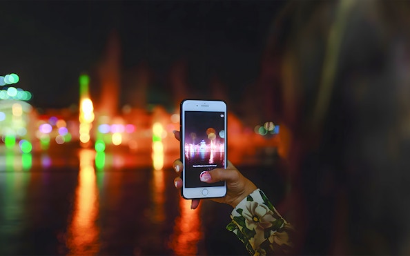 Hand holding a phone capturing Dubai Water Canal lights during dinner cruise.