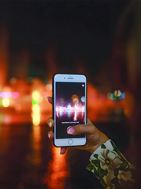 Hand holding a phone capturing Dubai Water Canal lights during dinner cruise.
