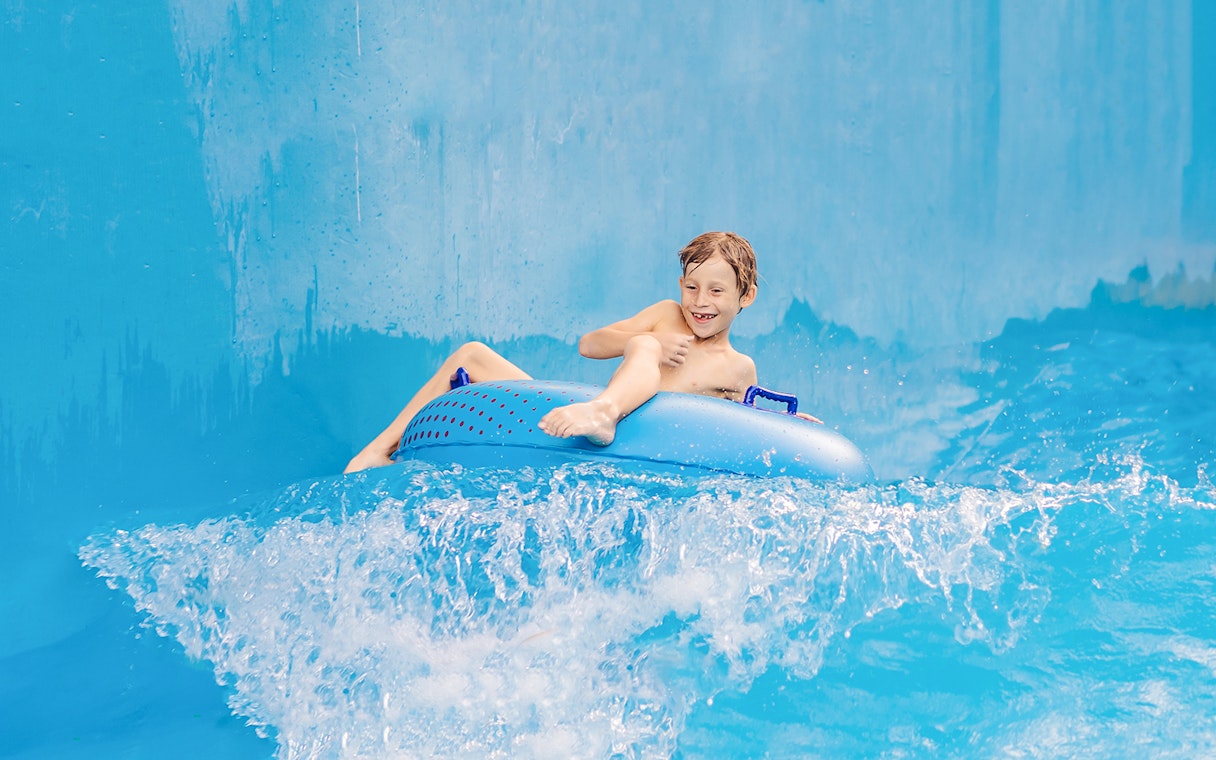 Boy enjoying a ride on a blue pool float in a water park.