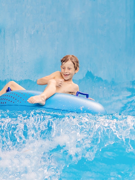 Boy enjoying a ride on a blue pool float in a water park.