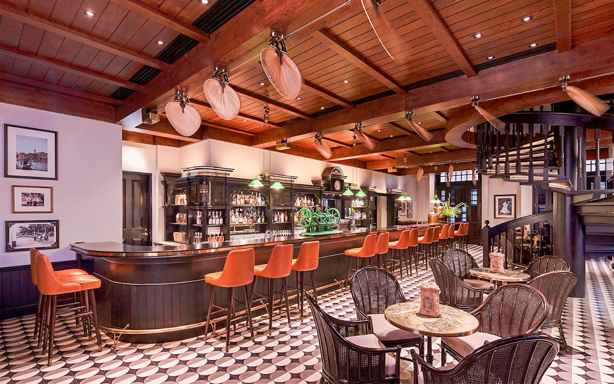 Bar interior with wooden ceiling, spiral staircase, and orange bar stools in Singapore.