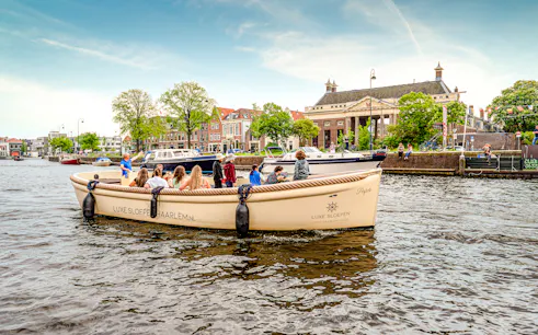 Open boat tour on Haarlem canal with passengers enjoying city views.