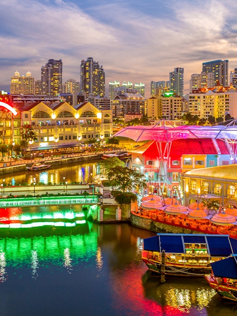 Singapore River Cruise with vibrant Clarke Quay lights and city skyline at dusk.