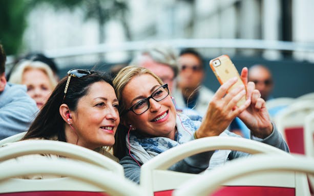 Tourists taking a selfie on a hop-on hop-off bus tour.
