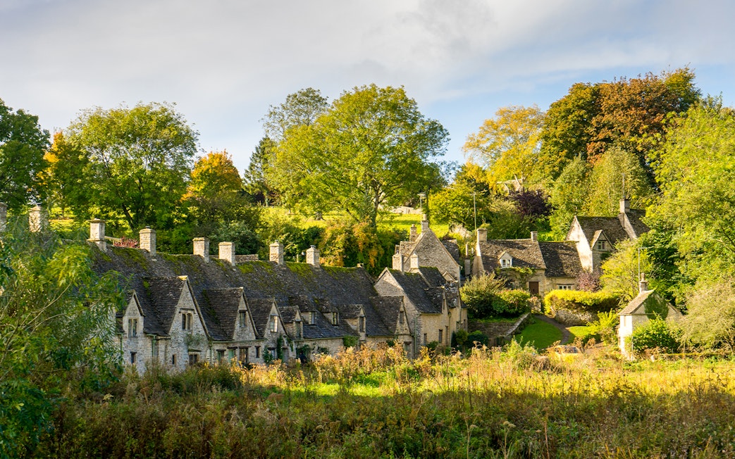Stone cottages in a Cotswolds village surrounded by lush greenery.