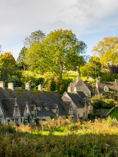 Stone cottages in a Cotswolds village surrounded by lush greenery.