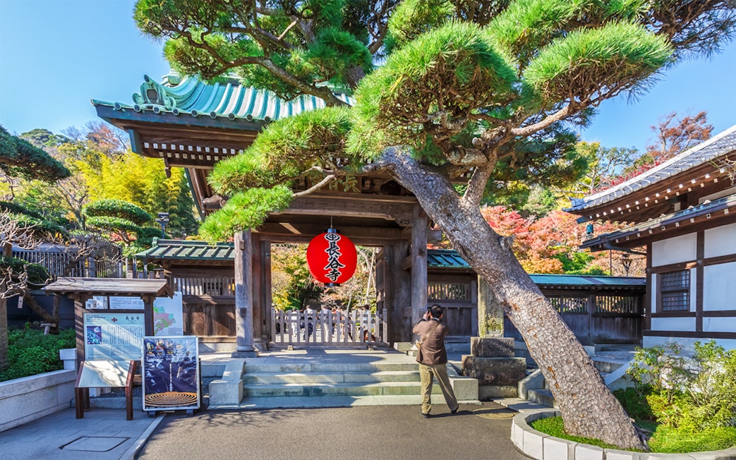 Kamakura Hasedera Temple entrance with red lantern and visitor taking photos.