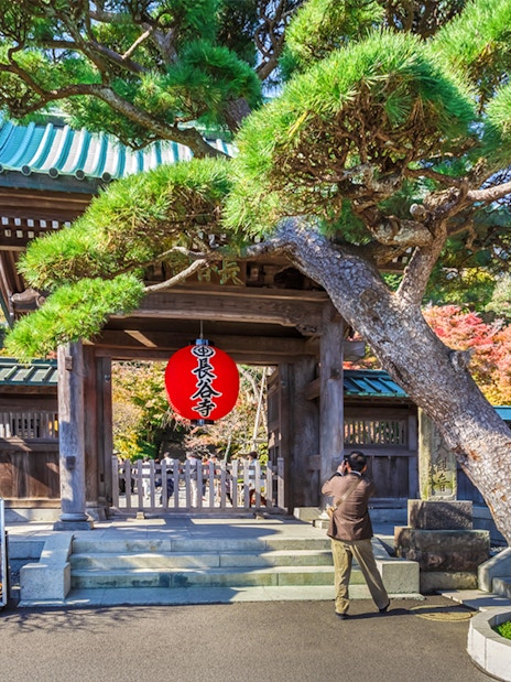 Kamakura Hasedera Temple entrance with red lantern and visitor taking photos.