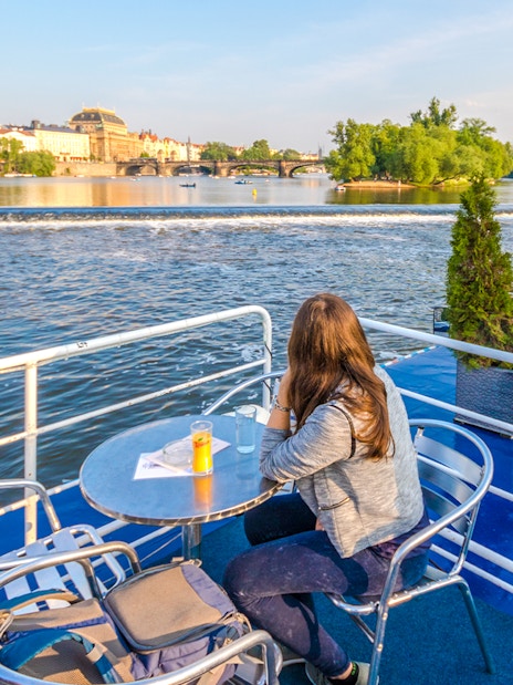 Person enjoying Vltava River view from a cruise deck in Prague.