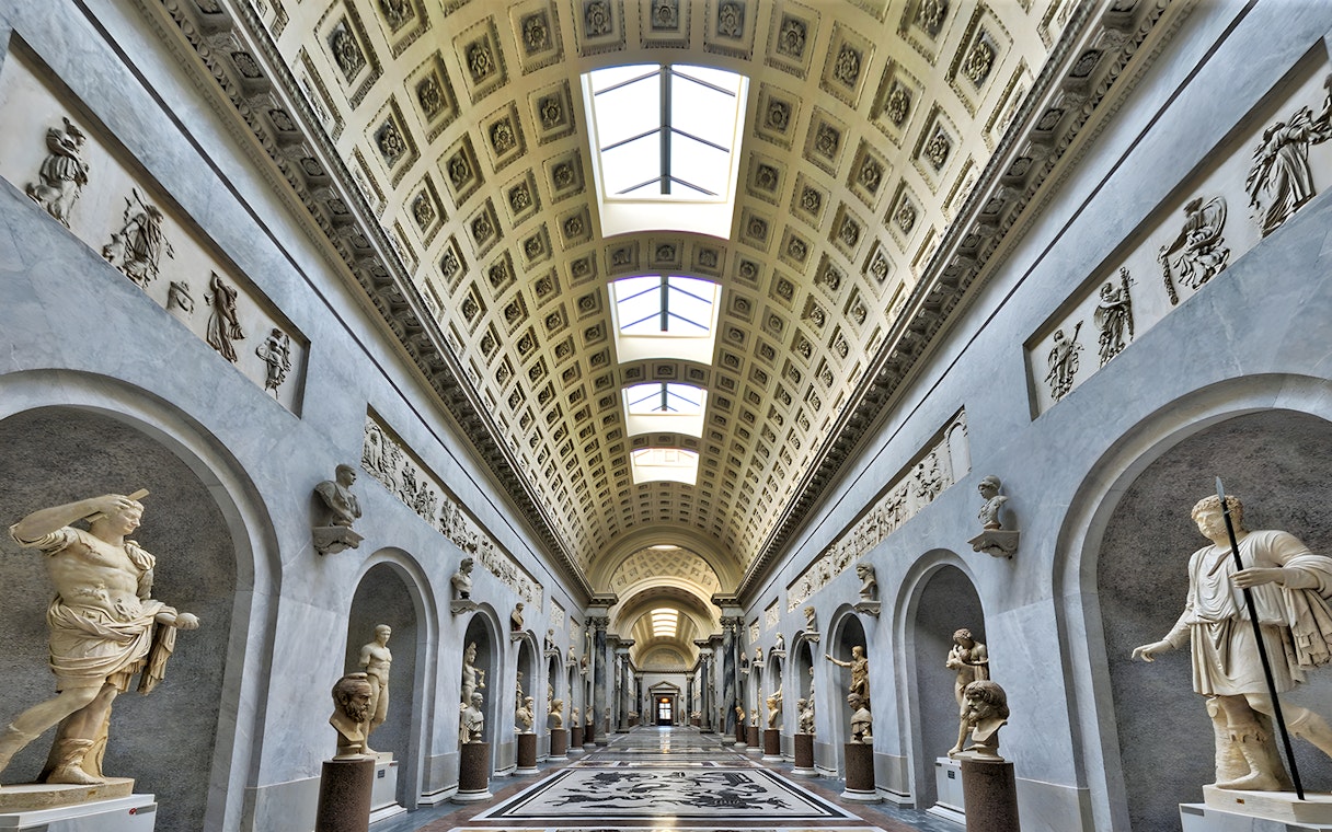Vatican Museum gallery with classical statues and ornate ceiling.