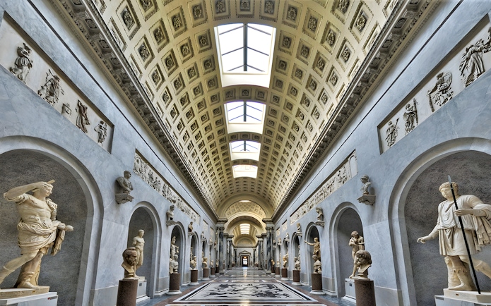Vatican Museum gallery with classical statues and ornate ceiling.
