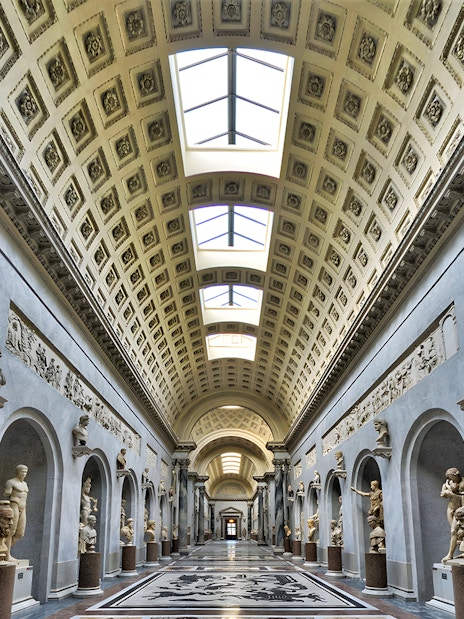 Vatican Museum gallery with classical statues and ornate ceiling.