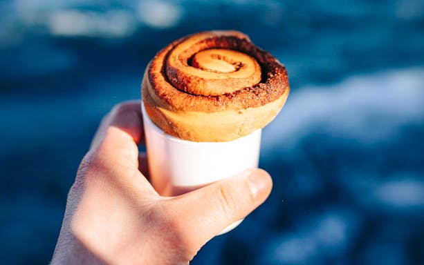 Hand holding hot chocolate with a cinnamon bun on a whale watching cruise in Iceland.