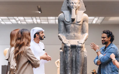 Guests engaging with a guide near an ancient statue at Louvre Museum Abu Dhabi.