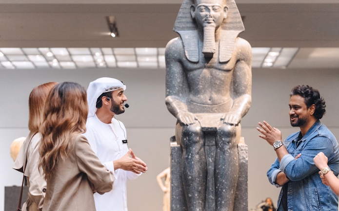 Guests engaging with a guide near an ancient statue at Louvre Museum Abu Dhabi.