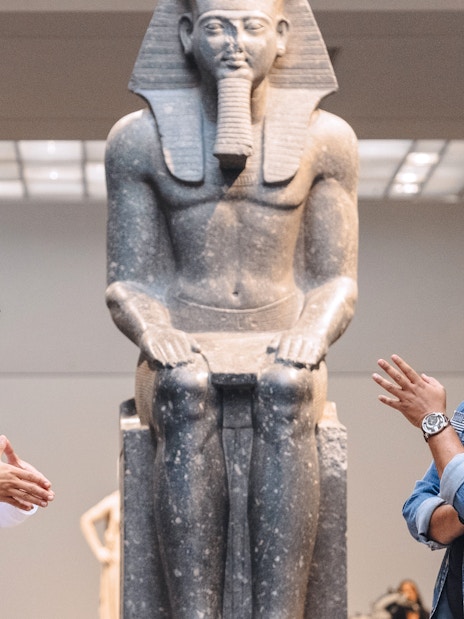 Guests engaging with a guide near an ancient statue at Louvre Museum Abu Dhabi.