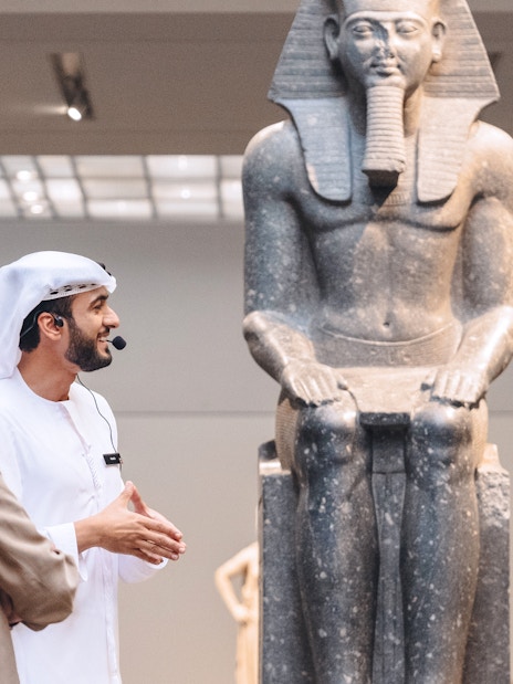 Guests engaging with a guide near an ancient statue at Louvre Museum Abu Dhabi.