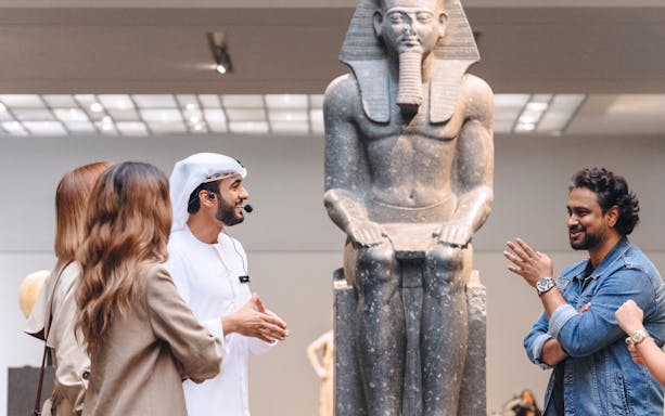 Guests engaging with a guide near an ancient statue at Louvre Museum Abu Dhabi.