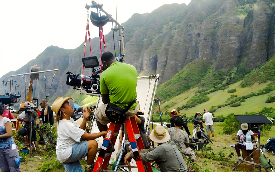 Film crew setting up equipment at Kualoa Ranch, Hawaii with lush mountains in the background.
