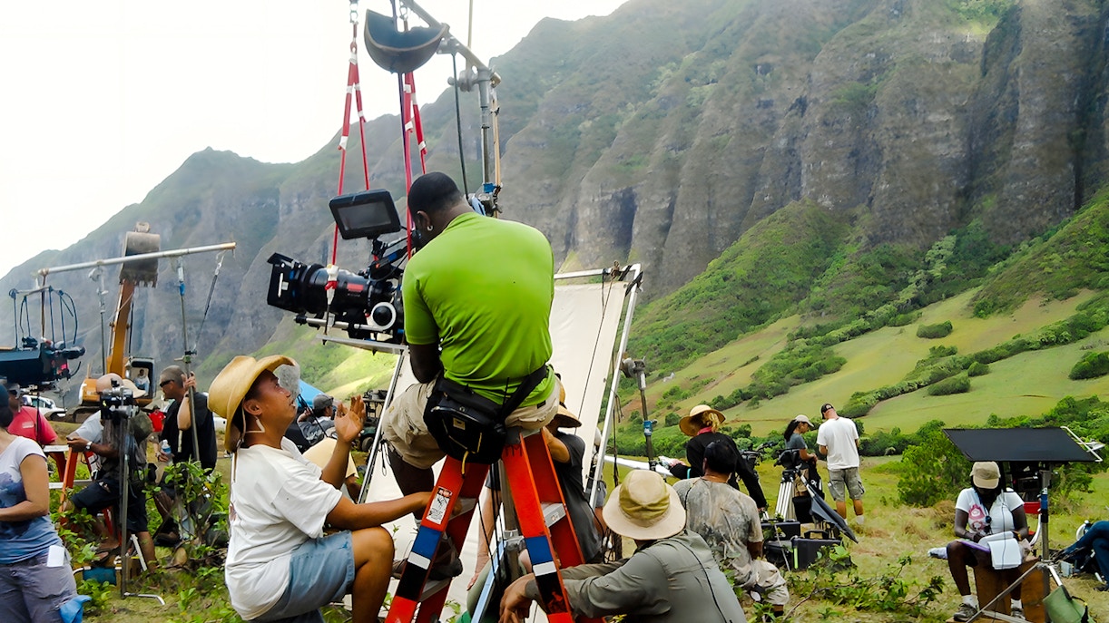 Film crew setting up equipment at Kualoa Ranch, Hawaii with lush mountains in the background.