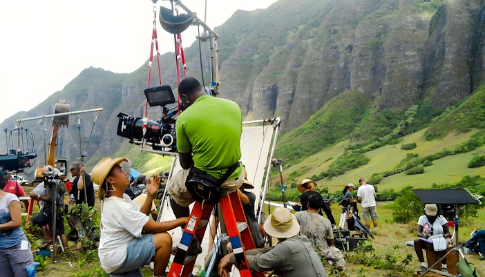 Film crew setting up equipment at Kualoa Ranch, Hawaii with lush mountains in the background.