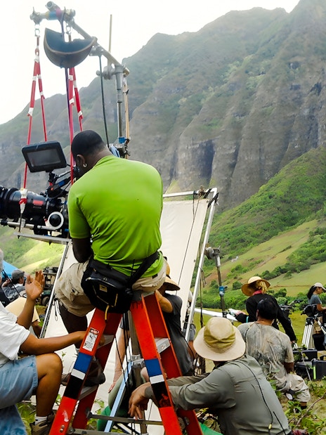 Film crew setting up equipment at Kualoa Ranch, Hawaii with lush mountains in the background.