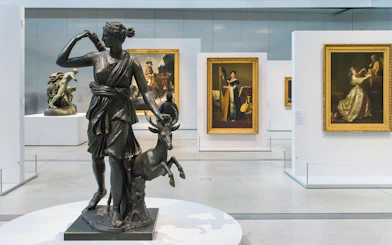 Sculpture of Diana with deer in Louvre Museum gallery, surrounded by classic paintings.